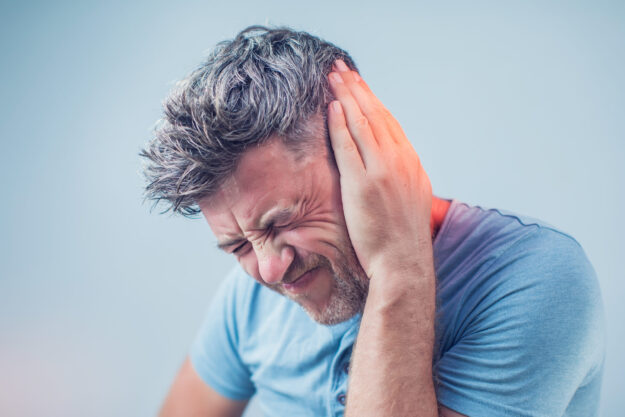 male having ear pain touching his painful head isolated on gray background